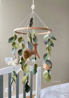 a baby crib with an animal mobile hanging from it's side and leaves on the bottom