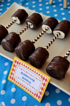 chocolate covered marshmallows sitting on a plate with candy sticks in the middle