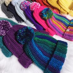 several knitted hats are lined up on a white furnishing area, one is multicolored and the other has a pom