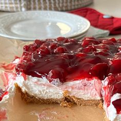 a piece of cheesecake covered in cherries on top of a table next to a plate