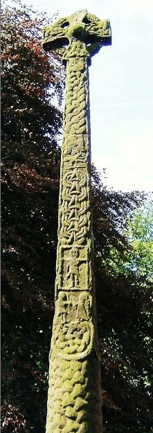 a large stone cross with writing on it in front of some trees and bushes behind it