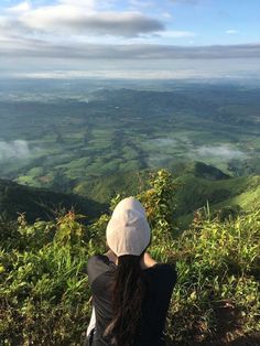 a woman sitting on top of a lush green hillside next to a forest filled valley