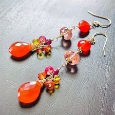 Gold filled statement earrings in stunning vibrant fiery red and orange hues. They are created with beautiful, exquisite quality carnelian briolettes and coins, petite coins of deep red garnet and delicately colored, plump in size, peach sapphire roundels wrapped in gold filled wire and arranged into attractive, long dangles. They are further embellished with small clusters of colorful sapphires above the carnelian briolettes.  Completed with gold filled ear wires these earrings measure 2.75 inches top to bottom. Perfect gift to brighten any occasion. Thank you for looking! Please contact me if you have any questions or requests. Free domestic First Class shipping. Shipping upgrade available. Gift wrap included and always free. Follow Agusha on Instagram @channahmorgenstern and Facebook: w Peach Sapphire, Orange Hues, Green Gems, Red And Orange, Fiery Red, Earrings Red, Colorful Earrings, Lovely Earrings, Red Garnet