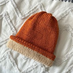 an orange and white knitted hat laying on top of a bed