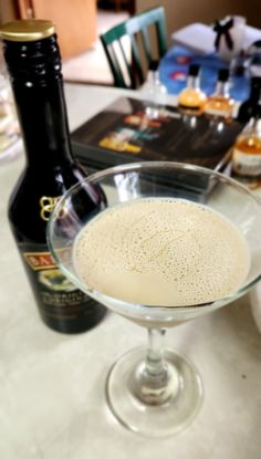 a glass filled with liquid sitting on top of a table next to bottles and glasses