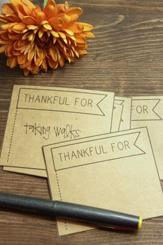 three cards with words written on them sitting next to a pen and orange flower in the background