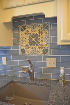 a kitchen sink with blue and yellow tiles on the backsplash, above it is a stainless steel faucet