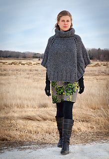 a woman standing in the middle of a field wearing a gray ponchot and black boots