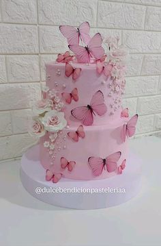 a three layer pink cake with butterflies and flowers on the top, sitting in front of a white brick wall