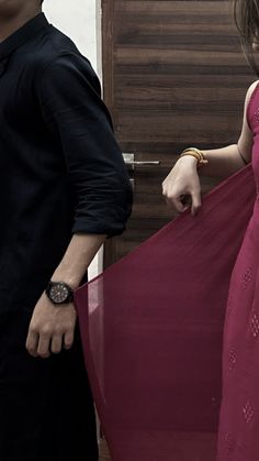 a man and woman standing next to each other in front of a wooden door holding an umbrella