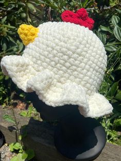 a white crocheted hat with red, yellow and blue flowers on it sitting on top of a wooden bench