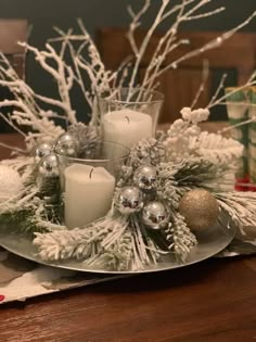 a christmas centerpiece with white candles and silver ornaments on a wooden dining room table