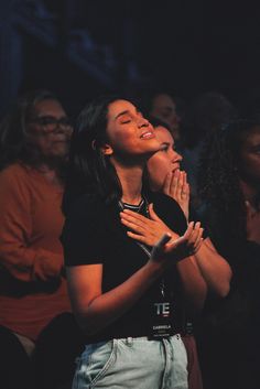 two women are praying in the dark with their hands together and people looking up at them