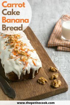 carrot cake with white icing and chopped walnuts on a cutting board next to a glass of milk