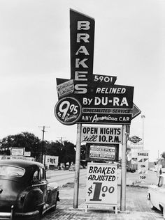 a black and white photo of an old car parked in front of a business sign