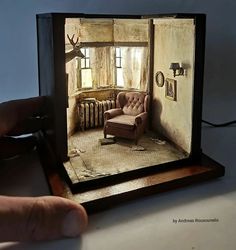 a person holding up a miniature photo of a living room with a chair and radiator