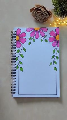 an open notebook with pink flowers and green leaves on it next to a pine cone