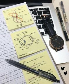 a watch, pen and notebooks on a desk next to a laptop with notes