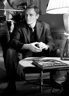 a black and white photo of a man in a suit sitting at a table with a camera