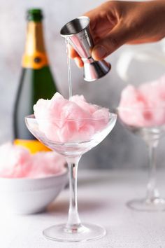 someone is pouring pink cotton into a martini glass with champagne in it and another bottle next to the glasses