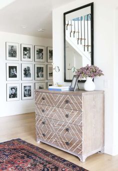 a dresser with flowers on top in front of a staircase and framed pictures behind it