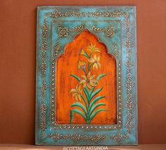 an orange and blue frame with flowers painted on the wall in front of a brown wall