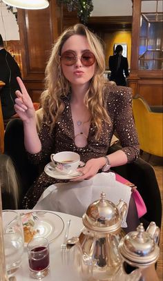 a woman sitting at a table with a tea pot and saucer in front of her