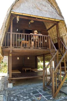 a woman standing on the balcony of a wooden house with stairs leading up to it