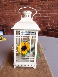 a white lantern sitting on top of a table with a sunflower in the center