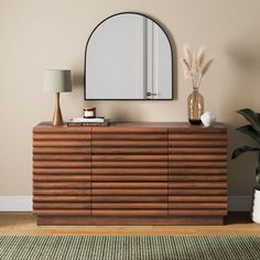 a wooden dresser with a mirror on top of it next to a plant and lamp