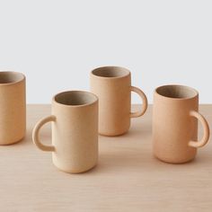 four coffee mugs sitting on top of a wooden table next to eachother