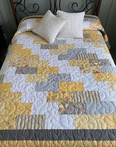 a bed with yellow and gray quilts on it