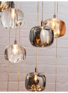 several glass lights hanging from the ceiling in a room with white brick wall behind them