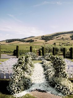 an outdoor ceremony setup with white flowers and greenery on the ground, surrounded by hills