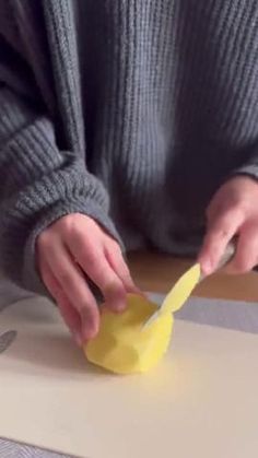 a person cutting paper with a knife and yellow object in front of them on a table