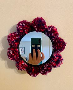 a hand holding a cell phone in front of a mirror with red and pink flowers on it