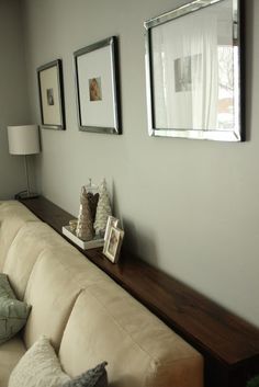 a couch sitting under a window next to a wooden shelf with pictures on top of it