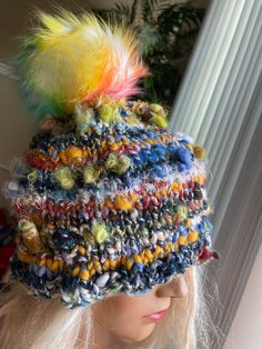 a woman wearing a multicolored knitted hat with feathers on it's brim