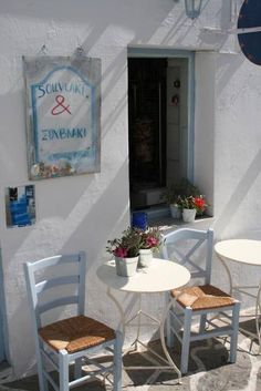 two chairs and a table with potted plants on the outside of a white building