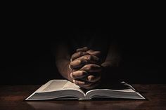 a person holding their hands over an open book on a wooden table in the dark