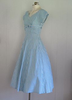 DESCRIPTION 1950s cotton dress Blue and white gingham Wide v-neck embellished with rhinestones and beads Under bust bow Fitted bodice/waist and full skirt Hand made Narrow white rick rack trim APPROXIMATE MEASUREMENTS (INCHES): Bust: 33 Waist: 26 Hip: OPEN Bodice (shoulder to waist): 15 Skirt (waist to hem): 30 CONDITION Excellent/very good. The under arms on both sleeves have been repaired/reinforced. Aside from this, the dress appears unworn. Vintage Dresses 50s Casual, Vintage 1950s Dress, Vintage Gingham Dress, 1950s Dress Casual, Vintage Gingham Dress For Garden Party, Classic Gingham Cotton Dresses, Gingham Cotton Dress, 1950s House Dress, Cotton V-neck Dress For Picnic