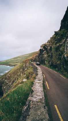 the car is driving down the road by the water's edge, near some cliffs