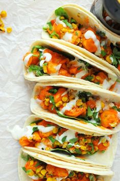 four tacos are stacked on top of each other with sauce and vegetables in them