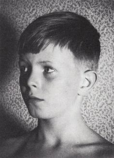 black and white photograph of a young boy with short hair looking at the camera while standing in front of a leopard print wall