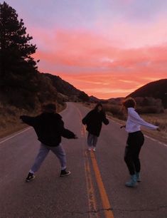 three people skateboarding down an empty road at sunset