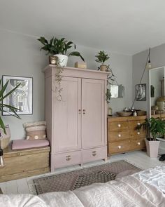 a bedroom with pink furniture and potted plants on top of the dresser next to it