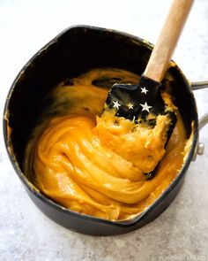 a wooden spatula filled with yellow sauce on top of a white counter next to a black pan