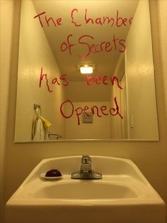 a bathroom mirror with writing on it and a sink in the foreground that says, the chamberber of secrets has been opened