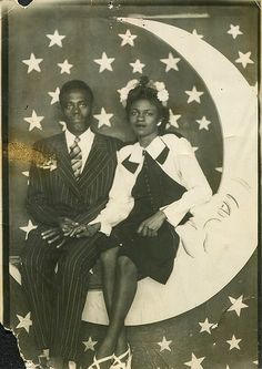 an old black and white photo of two people sitting on the moon with stars around them