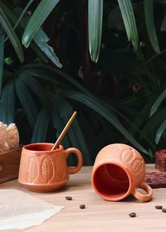 two ceramic mugs sitting on top of a wooden table next to some coffee beans